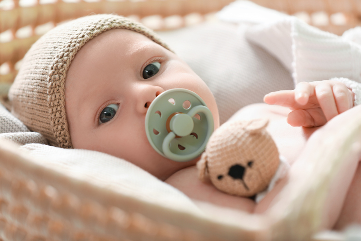 Photo shows newborn baby on white blanket in wicker crib, closeup