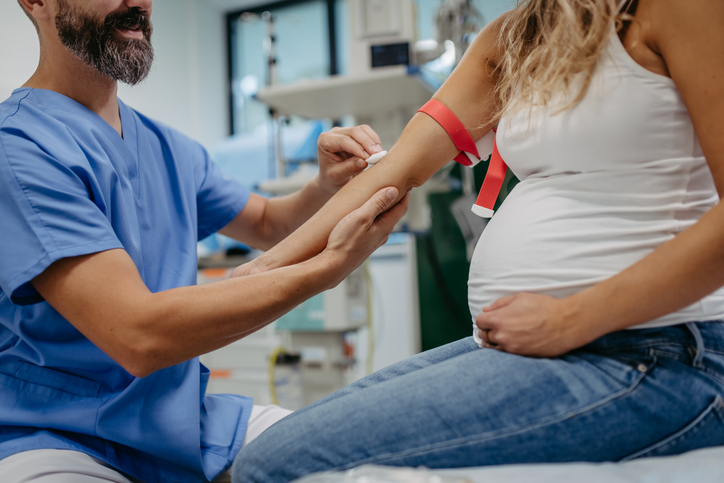 Photo shows physician taking blood sample from pregnant woman
