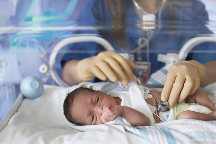 Photo shows doctor examining newborn baby in incubator