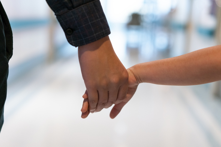 Photo shows father holding daughter's hand in a hospital corridor