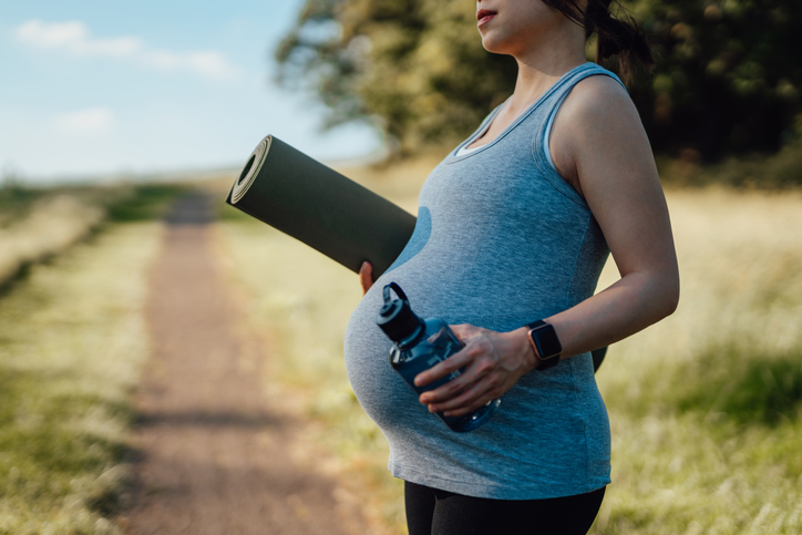 Photo shows a pregnant woman carrying yoga mat and water bottle