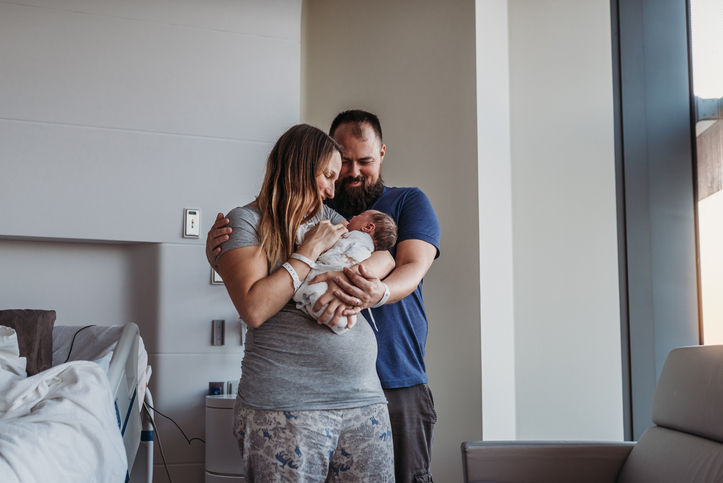 Photo shows Newborn baby being cradled by new parents in birthing center/Getty Images