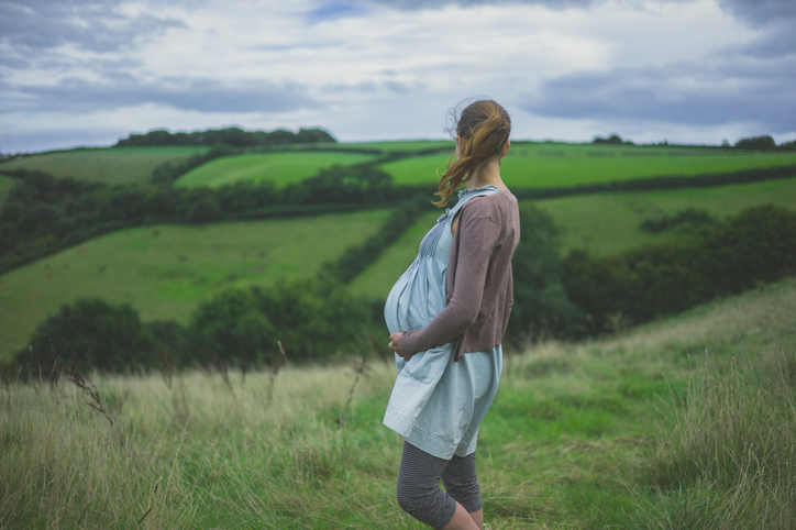 Photo shows a young pregnant woman standing in the countryside/Getty Images
