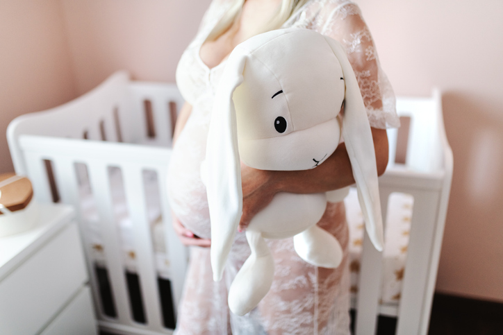 Photo shows a pregnant woman holding bunny toy while standing in baby room/Getty Images