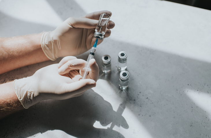 Photo shows a person wearing latex gloves holding a phial of clear liquid and a syringe/Getty Images