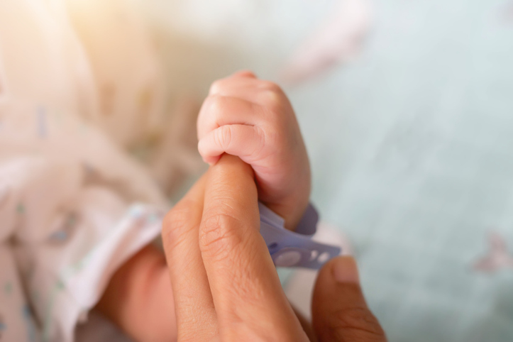 Photo shows an adult holding the hand of a newborn baby/Getty Images