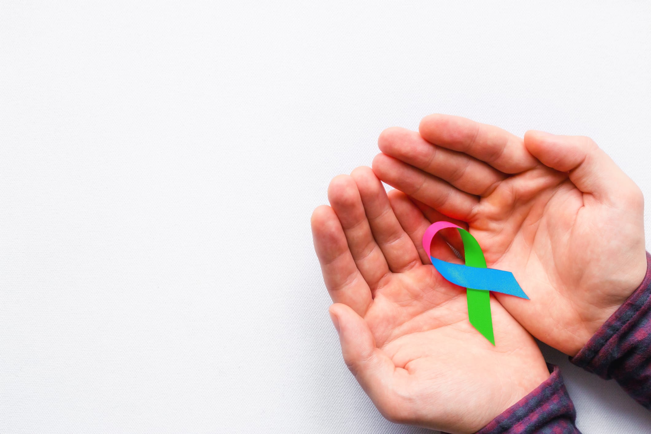Photo of hands holding pink, blue, and green ribbon of Rare Disease Day