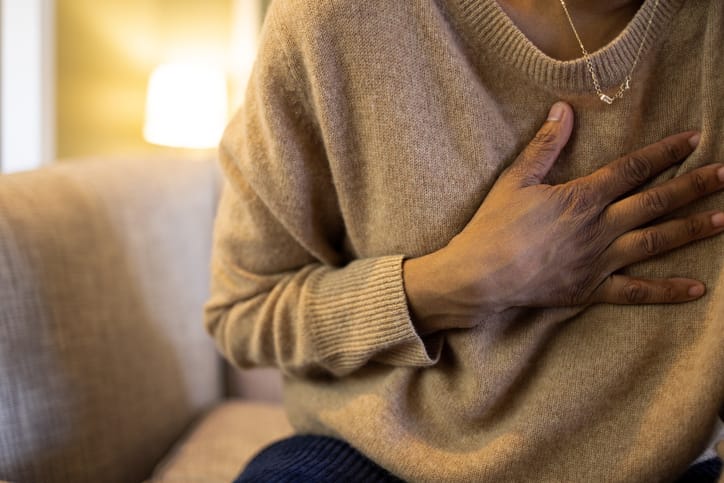 Photo shows a woman with chest pain sitting on her sofa/Getty Images