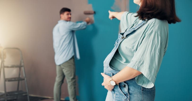 Photo shows a pregnant woman pointing at her partner while he paints a wall/Getty Images