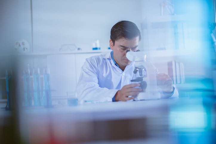 Photo shows a scientist in a lab coat examining a sample under a microscope/Getty Images